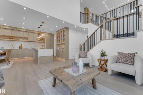 Open-concept living space with light wood-finish flooring, a contemporary kitchen, and a multi-level staircase - 206 Linden Loop, Leduc, AB 