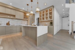 Modern kitchen featuring light-toned cabinetry, a waterfall island with slatted detailing, white countertops, and a white tile backsplash - 