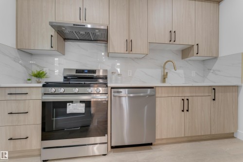 Modern kitchen featuring light wood-finish cabinetry with matte black hardware, white countertops, and a white tile backsplash - 206 Linden Loop, Leduc, AB 