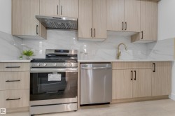 Modern kitchen featuring light wood-finish cabinetry with matte black hardware, white countertops, and a white tile backsplash - 