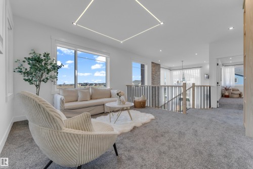 Bright open loft area with plush gray carpeting and a contemporary railing system featuring dark and light wood-tone spindles - 206 Linden Loop, Leduc, AB 
