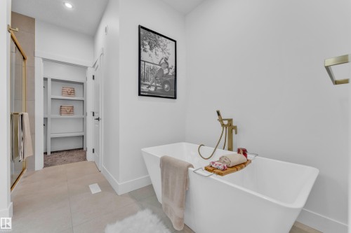 Freestanding soaking tub with a floor-mounted gold-finish faucet, tile flooring, and a glass-enclosed shower with gold-finish hardware - 206 Linden Loop, Leduc, AB 
