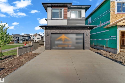 Modern contemporary exterior featuring a multi-textured facade, attached garage with stone-look cladding, concrete driveway, and a fenced side yard - 206 Linden Loop, Leduc, AB 