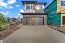 Modern contemporary exterior featuring a multi-textured facade, attached garage with stone-look cladding, concrete driveway, and a fenced side yard - 206 Linden Loop, Leduc, AB 