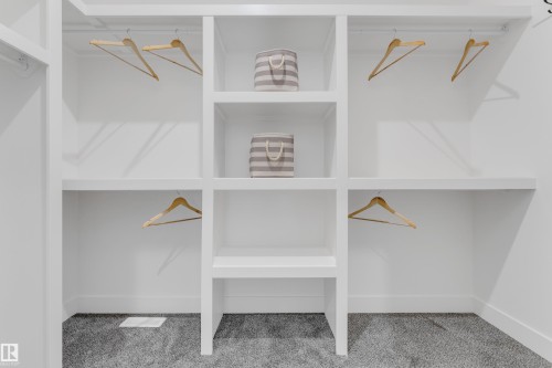Custom built-in closet system featuring white shelving, multiple hanging rods, and an integrated central shelving unit - 206 Linden Loop, Leduc, AB 