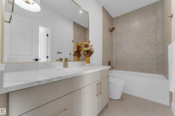 Bathroom featuring a single vanity with a white countertop and integrated sink, gold-toned fixtures, a framed mirror, a built-in bathtub, and floor-to-ceiling wall tiling in the shower area - 