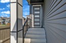Contemporary front entry featuring a dark gray door with frosted glass panels, concrete steps, and a black metal handrail - 206 Linden Loop, Leduc, AB 