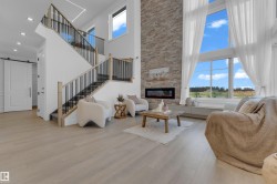 Two-story living area featuring a stone accent wall with an inset electric fireplace, soaring windows with sheer white drapes, and light wood-finish flooring - 