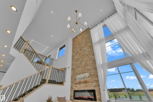 Two-story living area featuring a brick fireplace wall, a modern linear electric fireplace, and a striking tall window array - 206 Linden Loop, Leduc, AB 