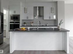 Kitchen island with dark countertop, white cabinetry, built-in stainless steel appliances, pendant lighting, and wood-finish flooring - 
