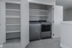 Integrated laundry area featuring a side-by-side washer and dryer, built-in shelving, white bifold doors, and light gray carpeting - 