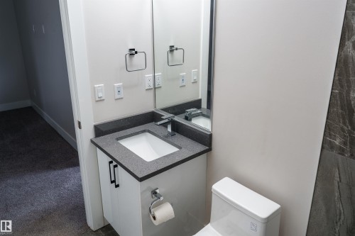 Modern bathroom vanity featuring a dark speckled countertop, undermount sink, and contemporary faucet - 2104 160 Street Sw, Edmonton, AB 
