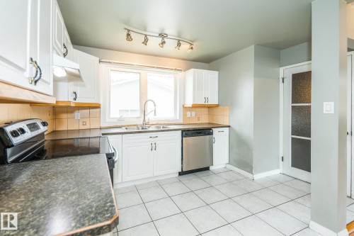 Kitchen featuring white cabinetry, tile backsplash, stainless steel dishwasher, track lighting, and a window above the sink - 7543 149A Avenue, Edmonton, AB 