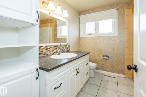 Bathroom featuring a white vanity with dark countertop, integrated sink, and mosaic tile backsplash - 7543 149A Avenue, Edmonton, AB 