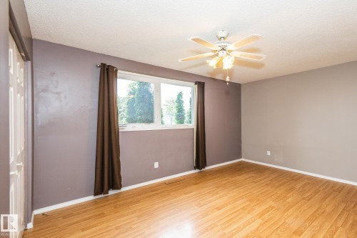 Room featuring wood-finish flooring, a ceiling fan with integrated lighting, and a window with exterior tree scenery - 7543 149A Avenue, Edmonton, AB 