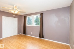 Room featuring wood-finish flooring, a ceiling fan with integrated lighting, a window with exterior tree scenery, and bi-fold closet doors - 