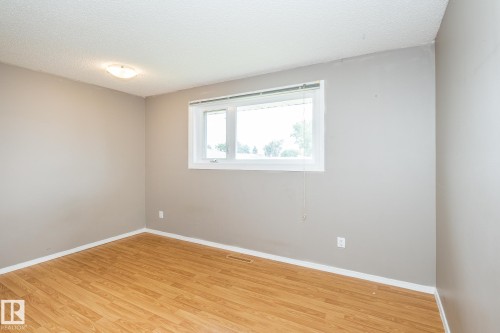 Room featuring wood-finish flooring, neutral gray wall tones, and a single window with white trim - 7543 149A Avenue, Edmonton, AB 