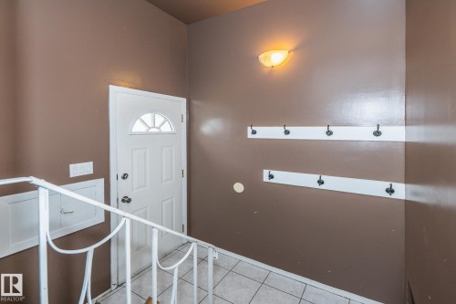 Entryway featuring a white paneled door with a sunburst-patterned window, white tiled flooring, and a white metal handrail - 7543 149A Avenue, Edmonton, AB 