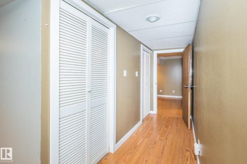 Hallway featuring wood-finish flooring, two sets of louvered bifold closet doors, neutral wall paint, and a recessed ceiling light - 7543 149A Avenue, Edmonton, AB 