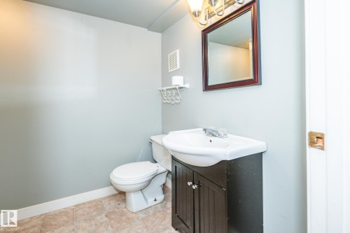 Bathroom featuring a dark wood-finish vanity with an integrated white sink, a framed mirror, and a three-bulb vanity light fixture - 7543 149A Avenue, Edmonton, AB 