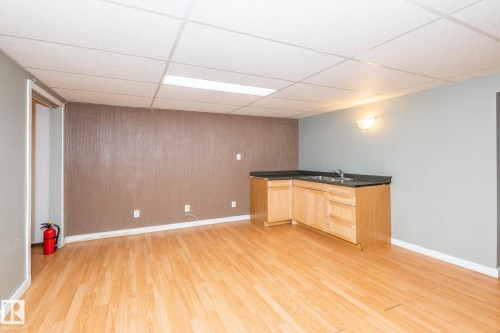 Spacious room featuring wood-finish flooring, a drop ceiling with recessed lighting, and a corner wet bar with light wood cabinetry, a sink, and dark countertops - 7543 149A Avenue, Edmonton, AB 