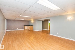 Spacious lower-level room featuring wood-finish flooring, a built-in wet bar with a dark countertop and wood cabinetry, and recessed lighting - 