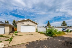 Detached garage with a white panel door, concrete driveway, stucco exterior, and gable roofline - 