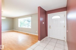 Entry foyer with tile flooring leading to a living area featuring wood-finish flooring, a large window, and a ceiling-mounted light fixture - 