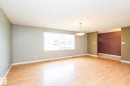 Spacious living area featuring wood-finish flooring, a large picture window, and a contemporary ceiling light fixture - 7543 149A Avenue, Edmonton, AB 