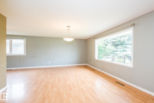 Spacious room featuring wood-finish flooring, light grey walls, and a large picture window - 7543 149A Avenue, Edmonton, AB 