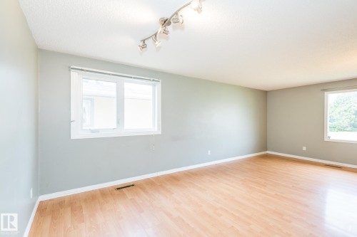 Spacious room featuring wood-finish flooring, light grey walls, and white trim - 7543 149A Avenue, Edmonton, AB 