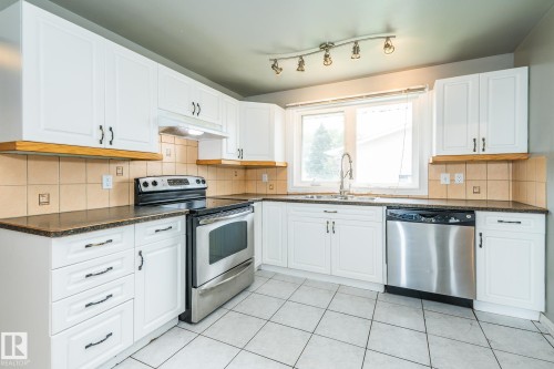 Bright kitchen featuring white cabinetry, dark countertops, a stainless steel range, and a stainless steel dishwasher - 7543 149A Avenue, Edmonton, AB 