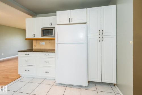Kitchen featuring white cabinetry, dark countertops, a tile backsplash, and a built-in microwave - 7543 149A Avenue, Edmonton, AB 