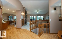 Open-concept interior featuring wood-finish flooring, a brick fireplace with a raised hearth, and natural wood railings - 