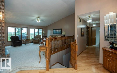Vaulted ceiling living area with large windows, brick fireplace, and plush carpeting - 60230 Rg Rd 271, Rural Westlock County, AB 