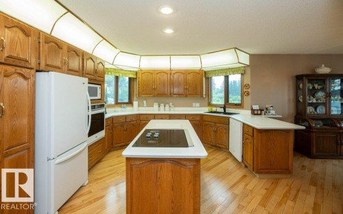 Kitchen featuring light wood-finish flooring, wood cabinetry, white countertops, a central island with an integrated cooktop, and built-in appliances - 60230 Rg Rd 271, Rural Westlock County, AB 