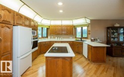 Kitchen featuring light wood-finish flooring, wood cabinetry, white countertops, a central island with an integrated cooktop, and built-in appliances - 