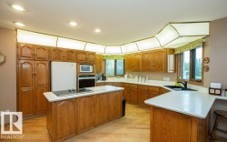 Kitchen featuring extensive wood cabinetry, light-toned countertops, a central island with a cooktop, integrated wall oven, and abundant natural light from multiple windows - 