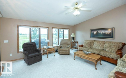 Bright living space featuring large windows with wood-finish trim, a ceiling fan with integrated lighting, and light-colored carpeting - 60230 Rg Rd 271, Rural Westlock County, AB 