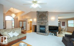 Expansive living area featuring a brick fireplace with a raised hearth, vaulted ceilings, and a crystal chandelier - 