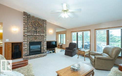 Spacious living area featuring a brick fireplace with a raised hearth, vaulted ceiling with a ceiling fan, and light-toned carpet flooring - 60230 Rg Rd 271, Rural Westlock County, AB 