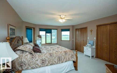 Carpeted room featuring a wood-finish bed frame, multiple windows with blue blinds, two wood-finish bi-fold closets, and a ceiling fan - 60230 Rg Rd 271, Rural Westlock County, AB 