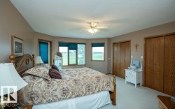 Carpeted room featuring a wood-finish bed frame, multiple windows with blue blinds, two wood-finish bi-fold closets, and a ceiling fan - 