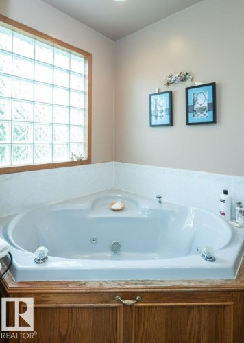 Corner soaking tub with a tiled surround, wood-finish paneling, and an integrated glass block window - 60230 Rg Rd 271, Rural Westlock County, AB 