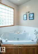 Corner soaking tub with a tiled surround, wood-finish paneling, and an integrated glass block window - 