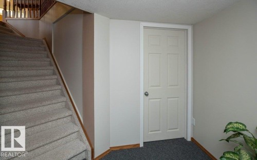 Carpeted stairway with a wooden handrail, white painted walls, and a six-panel interior door with a chrome knob - 60230 Rg Rd 271, Rural Westlock County, AB 