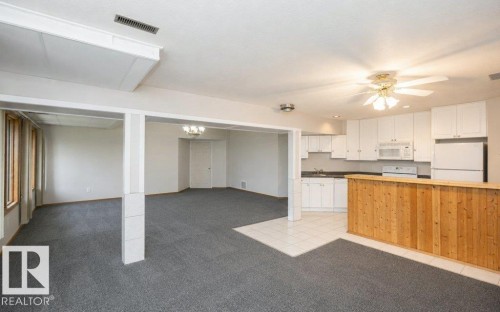 Open concept living area with grey carpet, a full kitchen featuring white cabinetry and appliances, and a wood-paneled bar - 60230 Rg Rd 271, Rural Westlock County, AB 