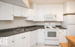 Kitchen featuring white cabinetry, dark countertops, a stainless steel sink, a range, and an over-the-range microwave - 