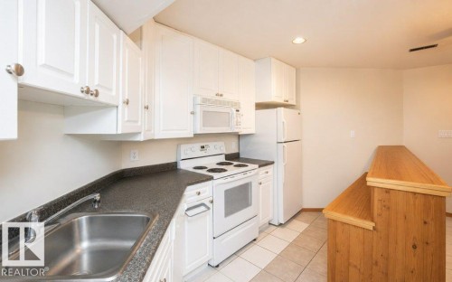 Kitchen featuring white cabinetry, dark speckled countertops, white appliances, a stainless steel sink, and a wood-finish breakfast bar - 60230 Rg Rd 271, Rural Westlock County, AB 