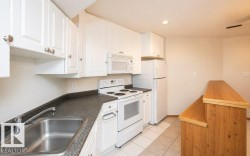 Kitchen featuring white cabinetry, dark speckled countertops, white appliances, a stainless steel sink, and a wood-finish breakfast bar - 